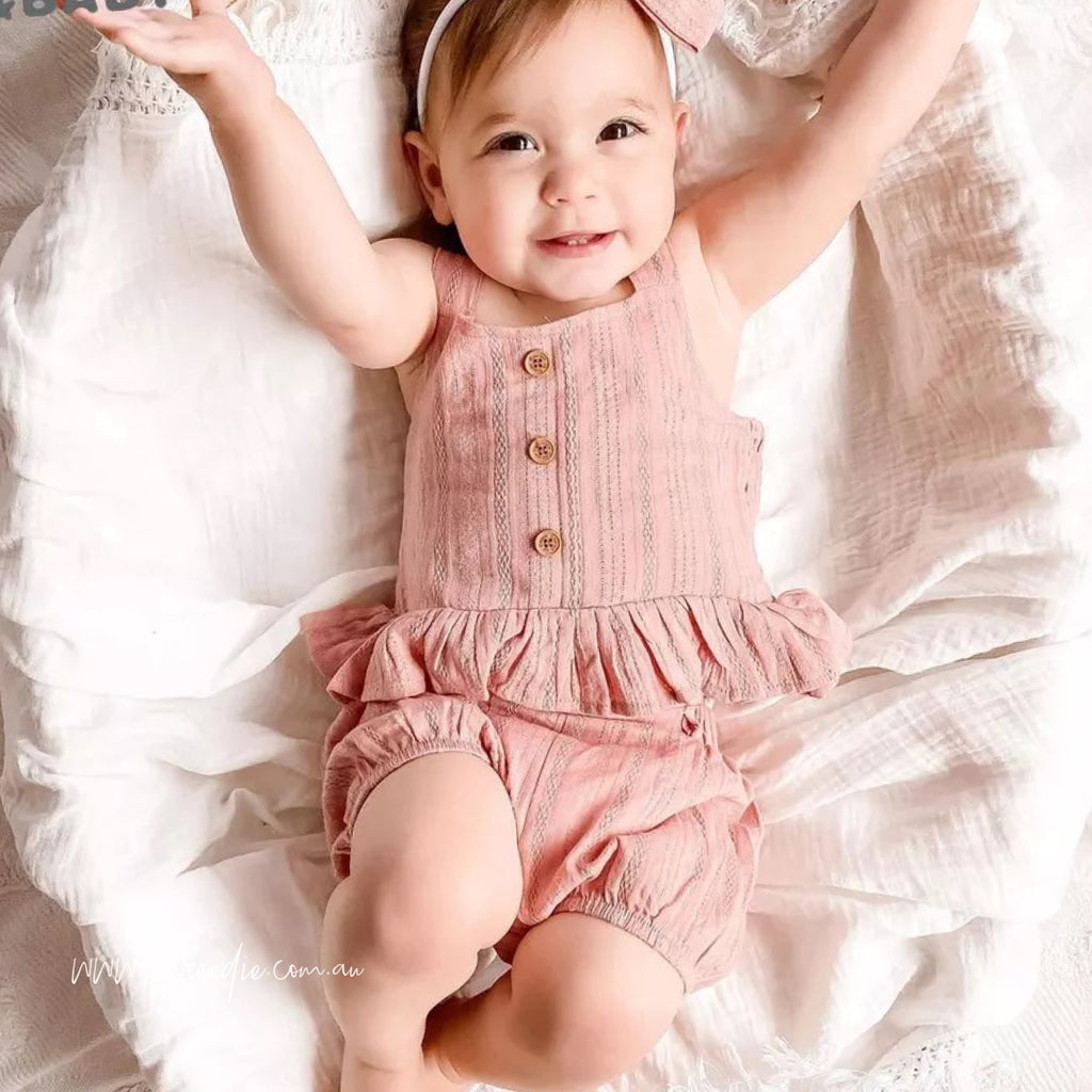 This is a photo of a baby girl wearing a pick outfit with little buttons on the top and matching shorts
